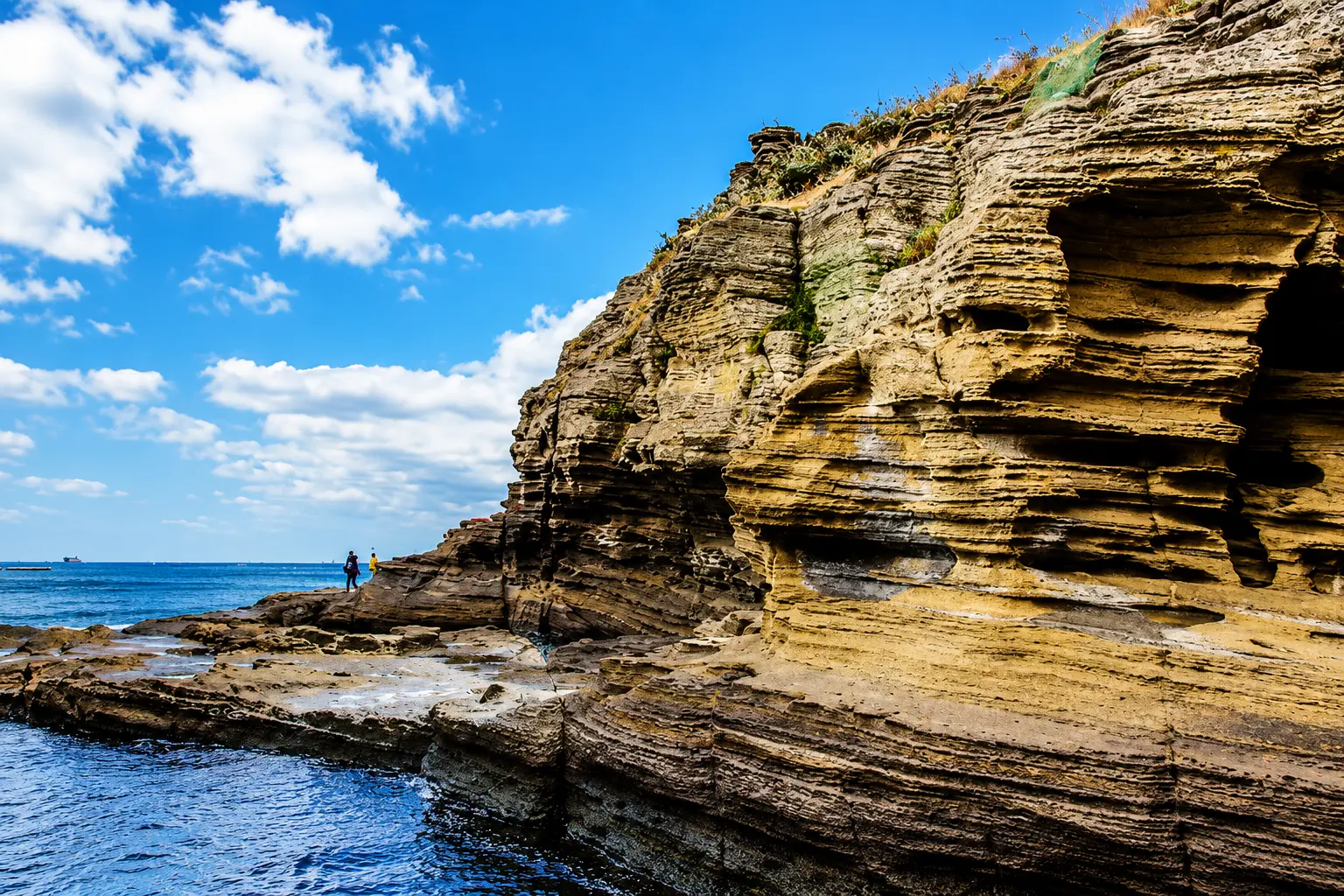 Layered volcanic rock cliffs meeting the sea on the Jeju coast